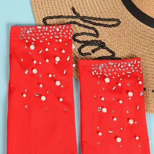 Dettaglio del tessuto della tuta rossa sexy decorato con strass lucidi e perle bianche