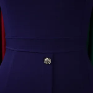 Gros plan sur le bouton argenté à blason à la taille d'une robe fourreau bleu marine.
