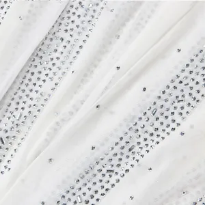 Close-up detail of white mesh fabric with shimmering hot-fix rhinestones for evening gowns
