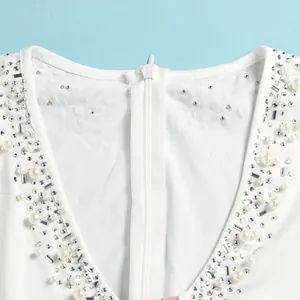 Dettaglio dello scollo a V della tuta bianca decorata con perle e strass trasparenti.