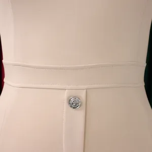 Détail d'une robe beige montrant le bouton lion argenté et la taille surpiquée