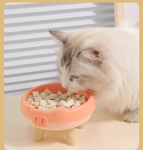 A fluffy white cat eating treats from a cute pink pig-shaped elevated pet food bowl