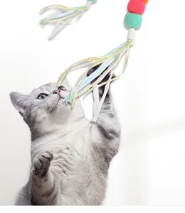 Gros plan d'un chat tigré gris jouant avec un jouet pour chat à pompons et rubans colorés.