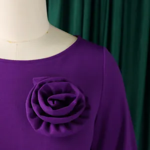 Détail d'une robe violette avec une grande rose en tissu décorative placée sur la poitrine.
