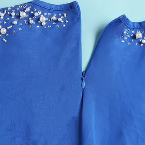 Dettaglio di una tuta blu con perle bianche, strass e cerniera lampo a scomparsa
