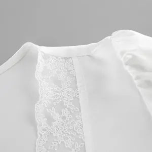 Close-up detail of white satin top featuring intricate lace stitching and floral patterns