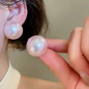 Detail shot of oversized pink iridescent pearl stud earrings on model ear and hand.