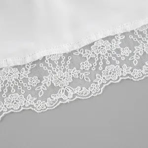Macro detail of white satin fabric with intricate floral lace trim on the hemline.