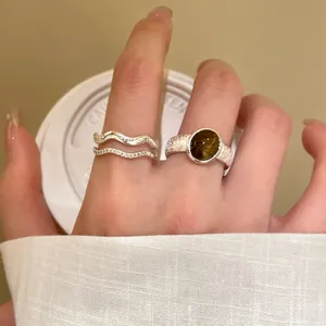 Detailaufnahme eines silbernen doppelten Wellenrings und eines grünen Edelsteinrings