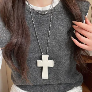 Close-up of white leather cross pendant with rose engraving on silver ball chain