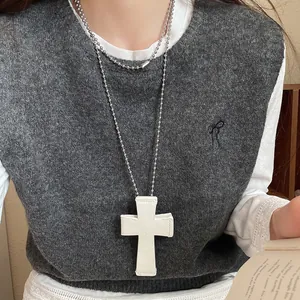 Close-up of a large white cross pendant on a silver beaded long sweater chain necklace