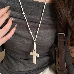 Close-up view of white stone beaded cross necklace in bohemian style on grey sweater