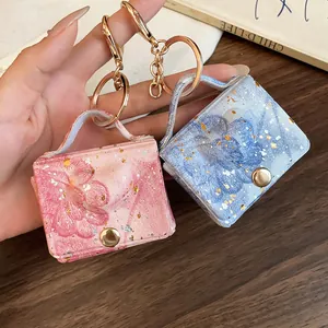 Dettaglio di mini portachiavi a forma di borsa in pelle con stampa floreale e oro
