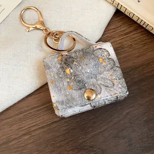 Dettaglio del portachiavi a forma di mini borsa stampata con accenti dorati