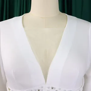 Detail shot of the V-neckline with mesh insert and beaded waist on a white jumpsuit