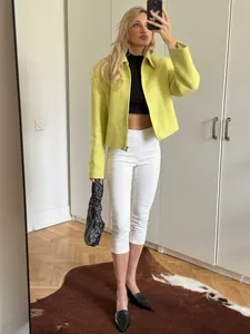 Full-body view of high-waisted white cropped yoga leggings styled with a green jacket