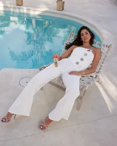 Detail eines eleganten weißen trägerlosen Jumpsuits mit weitem Bein und Metallknöpfen