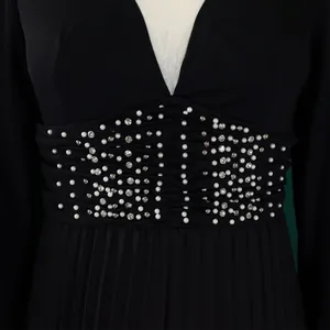 Close-up detail of white pearls and rhinestones on a pleated black jumpsuit waist