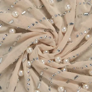 Detailansicht aus beige Netzstoff mit funkelnden Strasssteinen und eleganten weißen Perlen