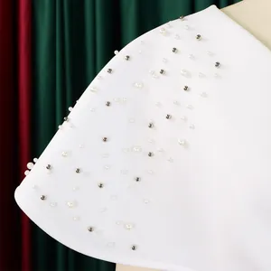 Close-up detail of white evening dress featuring elegant pearls and silver studs