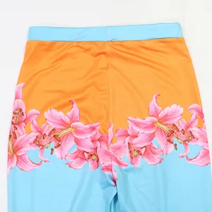 Close-up detail of the vibrant pink lily floral print on orange and blue high-waisted pants