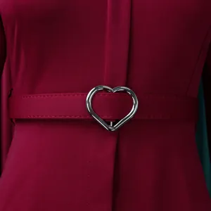 Gros plan sur la boucle de ceinture en forme de cœur argenté sur cette robe bordeaux.