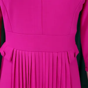 Détail en gros plan des plis structurés et du bouton à la taille d'une robe d'automne magenta