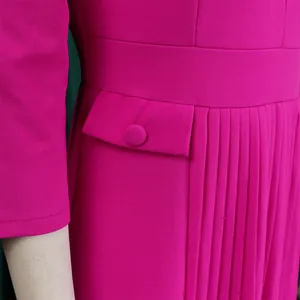 Détail d'une robe plissée magenta avec rabat de poche décoratif et bouton gainé.