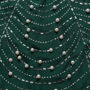 Detailaufnahme eines dunkelgrünen Kleides mit kunstvollen Strass- und Perlenverzierungen.