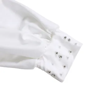 Close-up of white garment cuff with delicate pearl and rhinestone beadwork detail