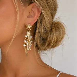 Primo piano elegante di orecchini dorati a forma di stella marina e pesci con perle su modella