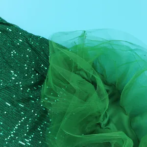 Detailed macro view of emerald green sequin fabric and mesh patchwork for evening dress
