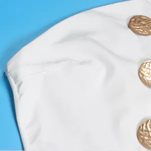 Detailansicht eines weißen Jumpsuits mit großen, gehämmerten goldenen Zierknöpfen als Akzent