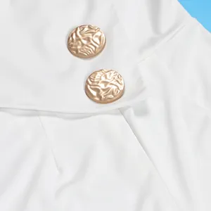Detaillierte Nahaufnahme strukturierter goldener Metallknöpfe auf einem weißen Jumpsuit-Stoff