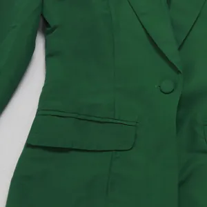 Nahaufnahme eines grünen Blazers mit Stofftextur, Taschenklappe und Knopf.