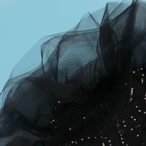 Macro detail of black sequined fabric with delicate pleated mesh ruffles on blue background.