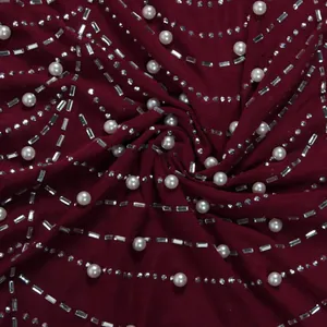 Detailaufnahme des weinroten Kleiderstoffs mit eleganten Perlen und glänzenden Strasssteinen.