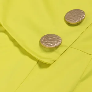 Nahaufnahme von neongelbem Stoff mit strukturierten goldenen Metallknöpfen am Overall