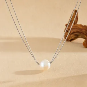 Détail d'une perle blanche naturelle sur une chaîne double en acier inoxydable argenté.