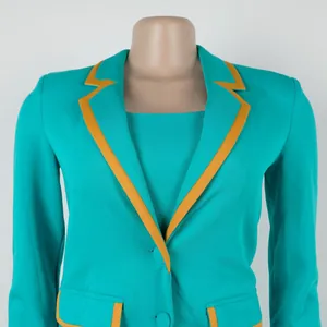 Detail view of an elegant teal blazer featuring yellow piping and a matching inner vest set