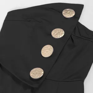 Detailaufnahme der goldenen Zierknöpfe an einem schwarzen ärmellosen Jumpsuit mit weitem Bein.