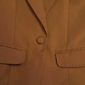 Detailansicht eines braunen Blazers mit Revers, bezogenem Knopf und Pattentaschen.