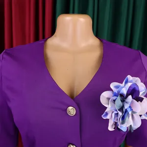 Dettaglio ravvicinato abito viola con scollo a V, fiore decorativo e bottone dorato