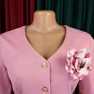 Dettaglio di un abito rosa con scollo a V, spilla floreale e bottoni dorati decorativi