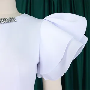 Close-up detail of a white party dress featuring a rhinestone neckline and layered ruffled sleeves
