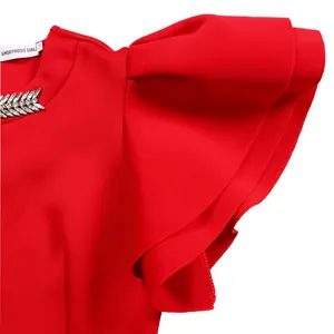 Close-up of red dress with elegant ruffle sleeves and rhinestone leaf detail at neckline.