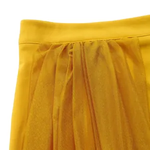 High-definition close-up detail of gathered yellow mesh fabric and smooth waistband of skirt