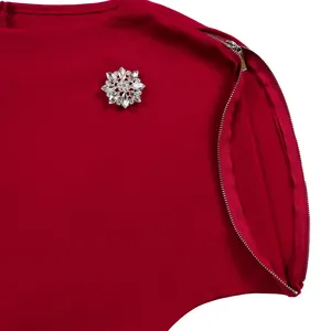 Dettaglio di un abito rosso con spilla di cristallo e cerniera sulla spalla.