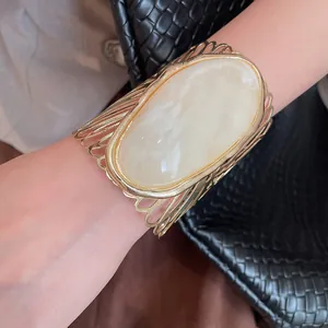 Close-up of a hollow gold metal cuff bracelet featuring a marbled cream stone.