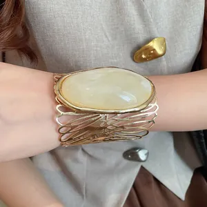 Detailed close-up showing a vintage gold hollow cuff bracelet with a large oval cream resin stone.
